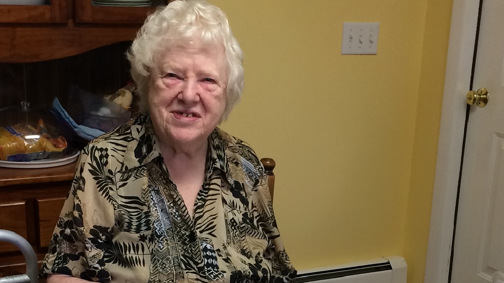 Photo of Dortha Shay, an elderly white woman with white hair, sitting at her dining room table